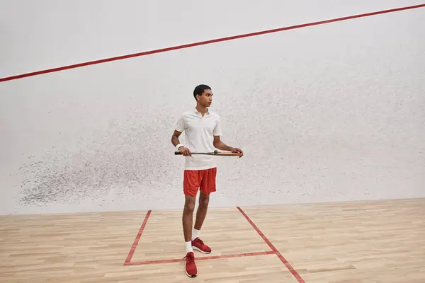 Deportista afroamericano sosteniendo pelota de squash y raqueta mientras juega dentro de la cancha - foto de stock