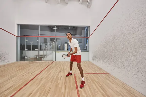 Jovem desportista afro-americano segurando bola de squash e raquete enquanto joga jogo dentro da quadra — Fotografia de Stock