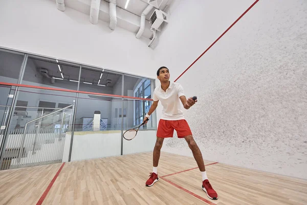 Ajustement sportif afro-américain tenant balle de squash et raquette tout en jouant à l'intérieur du court — Photo de stock