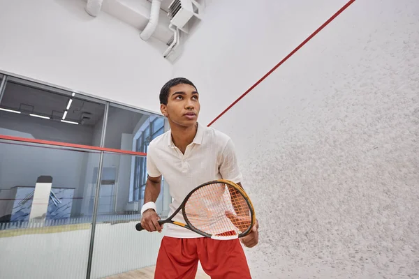 Atletico uomo africano americano che tiene racchetta da squash mentre gioca all'interno della corte — Foto stock