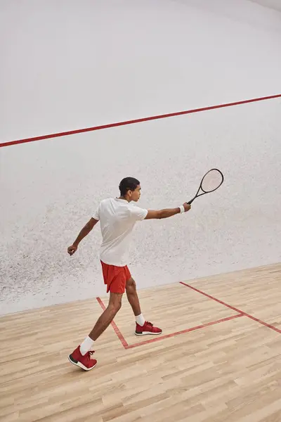 Atlético afro-americano desportista segurando squash raquete e pulando enquanto joga jogo na corte — Fotografia de Stock