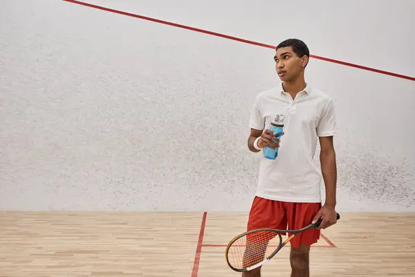 Athletic african american sportsman holding bottle of water and racquet after playing squash — Stock Photo