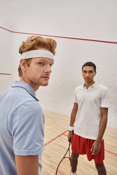 Fokussierte interrassische männliche Freunde in Sportbekleidung stehen zusammen mit Squash-Schlägern vor Gericht — Stockfoto