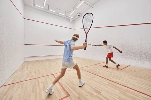 Deux joueurs multiculturels en vêtements de sport jouant au squash ensemble à l'intérieur du court, mode de vie actif — Photo de stock