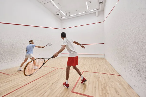 Amis multiculturels en vêtements de sport jouer au squash ensemble à l'intérieur de la cour, mode de vie actif — Photo de stock
