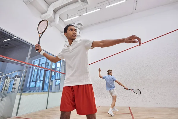 Interracial players in sportswear playing squash together inside of court, active lifestyle — Stock Photo