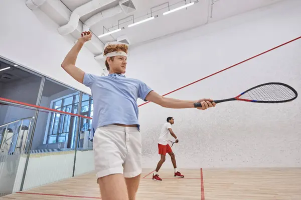 Joueurs interraciaux en vêtements de sport jouer au squash ensemble à l'intérieur du court, style de vie énergique — Photo de stock
