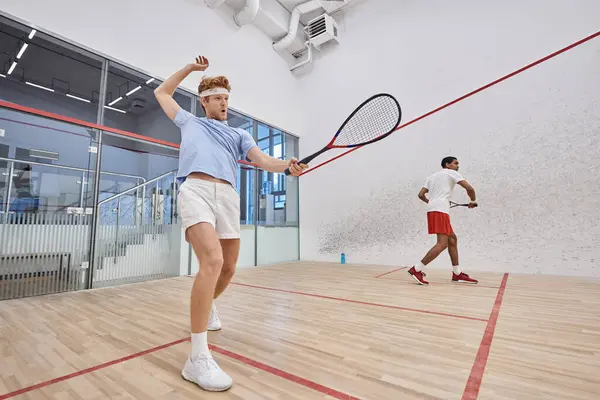 Interracial friends in sportswear playing squash together inside of court, motivation and sport — Stock Photo
