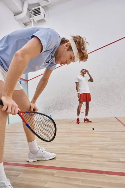 Cansados jugadores multiculturales en ropa deportiva respirando pesadamente después de jugar squash en la corte - foto de stock