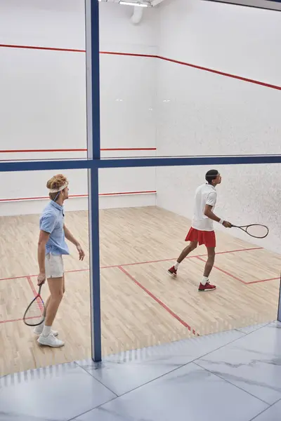 Amis multiculturels en vêtements de sport jouer au squash ensemble à l'intérieur du court, la motivation et le sport — Photo de stock