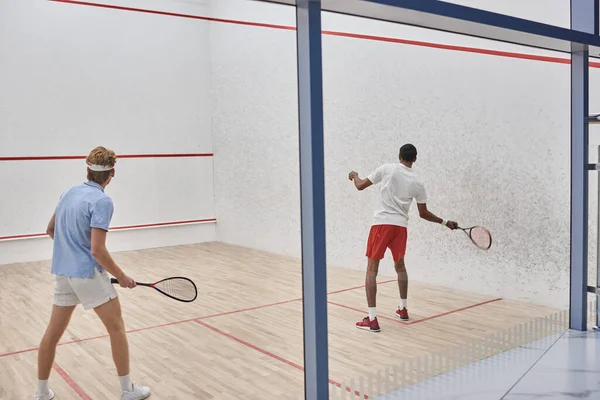 Joueurs multiculturels dans les vêtements de sport jouer au squash ensemble à l'intérieur du court, la motivation et le sport — Photo de stock