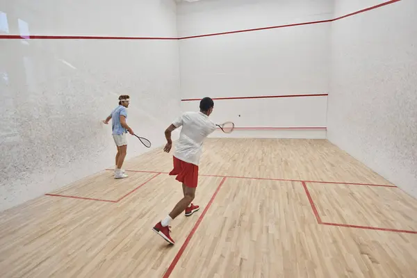 Multicultural friends in sportswear playing squash together in court, motivation and sport — Stock Photo