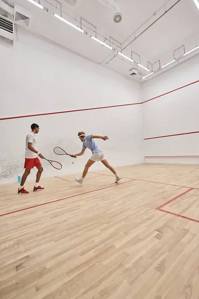 Interracial athletic men in sportswear playing together inside of squash court, motivation — Stock Photo