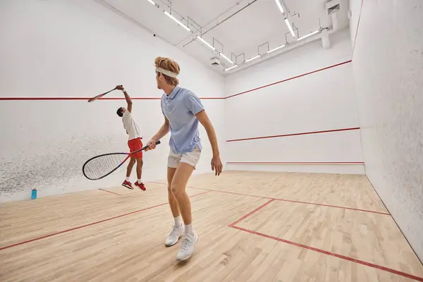 Hommes interraciaux en vêtements de sport jouant au squash ensemble à l'intérieur du court, fitness et motivation — Photo de stock
