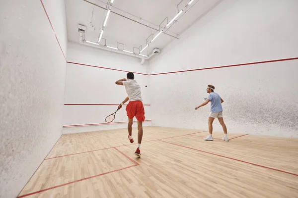 Joueurs interraciaux en vêtements de sport jouant au squash ensemble à l'intérieur du court, fitness et motivation — Photo de stock