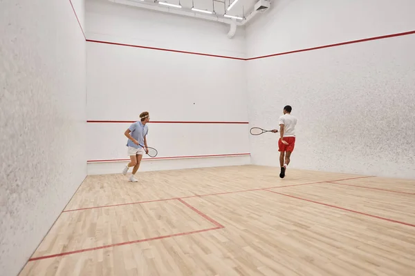 Active interracial sportsmen in sportswear playing squash inside of court, challenge and motivation — Stock Photo