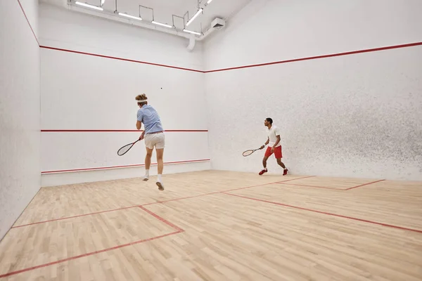 Athletic interracial men in sportswear playing squash inside of court, challenge and motivation — Stock Photo