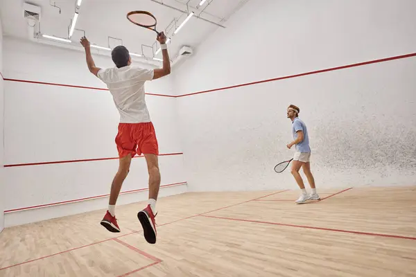 Joueurs interraciaux dans les vêtements de sport sauter et jouer au squash à l'intérieur du court, défi et motivation — Photo de stock