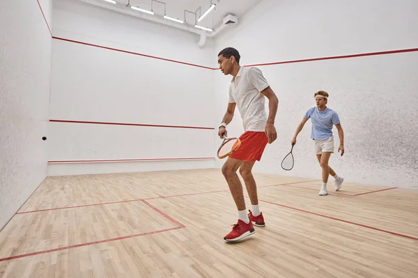 Young and active interracial men playing squash inside of court, challenge and motivation — Stock Photo