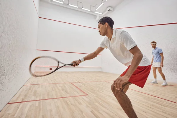 Young and active multicultural men playing squash inside of court, challenge and motivation — Stock Photo