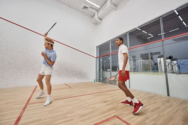 Sporty interracial men in sportswear playing squash inside of court, challenge and motivation — Stock Photo