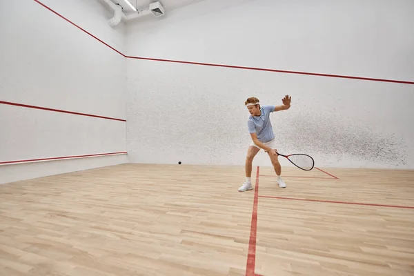 Joven y activo pelirrojo en ropa deportiva jugando squash dentro de la cancha, desafío y motivación - foto de stock