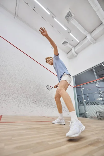 Joueur rousse actif dans le bandeau jouant au squash à l'intérieur du court intérieur, défi et motivation — Photo de stock