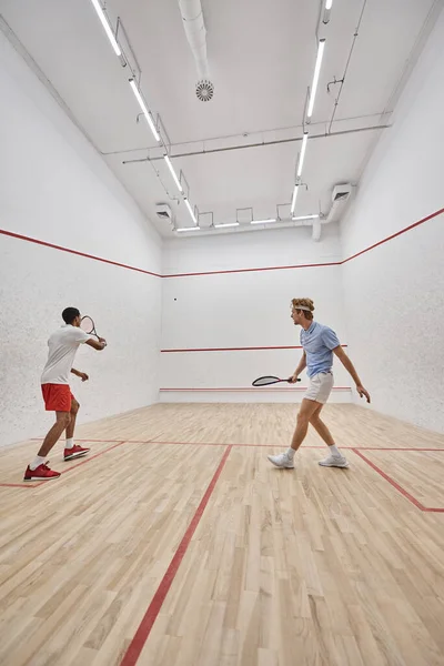 Dynamische interrassische Sportler spielen gemeinsam Squash innerhalb des Platzes, Teamwork — Stockfoto