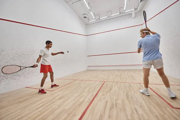 Dynamic and interracial friends playing squash together inside of court, challenge and motivation — Stock Photo