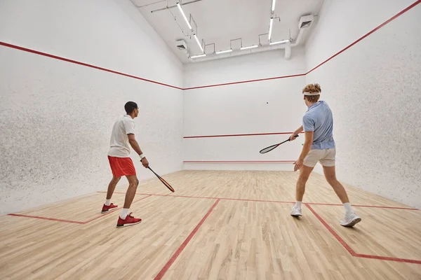 Dynamische und interrassische Freunde spielen gemeinsam Squash auf dem Court und bereiten sich auf den Wettkampf vor — Stockfoto
