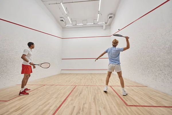 Active and interracial friends playing squash together inside of court, preparing for competition — Stock Photo