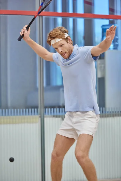 Energetic redhead sportsman holding racquet while playing squash inside of court, motion shot — Stock Photo