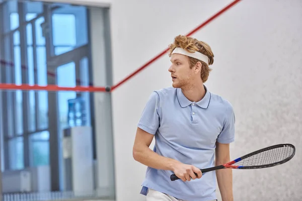 Athletic redhead sportsman holding racquet while playing squash inside of court, training shot — Stock Photo