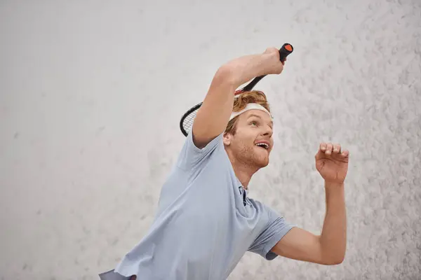 Active redhead sportsman holding racquet while playing squash inside of court, training shot — Stock Photo