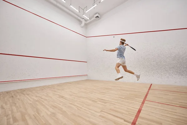 Atleta enérgico e ruivo segurando raquete e jogar squash dentro do tribunal, tiro movimento — Fotografia de Stock