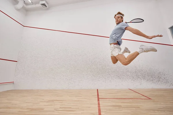 Tiro de movimento, atleta enérgico segurando raquete e pulando enquanto joga squash dentro do tribunal — Fotografia de Stock