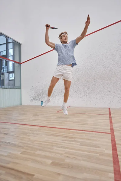Foto en movimiento, deportista divertido celebración de raqueta y saltar mientras juega squash dentro de la cancha - foto de stock