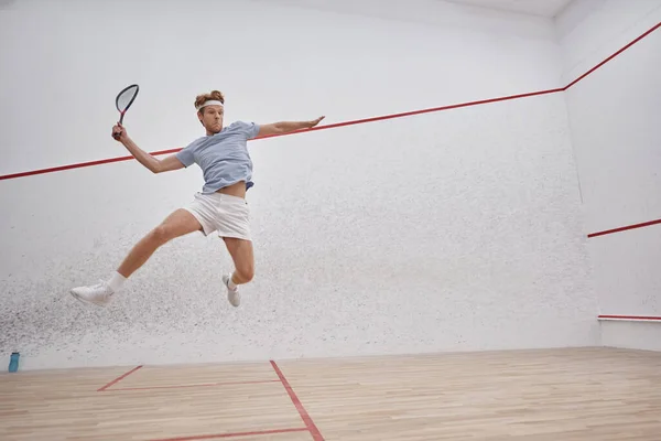 Coup de mouvement, sportif tenant la raquette et sautant tout en jouant au squash à l'intérieur du court — Photo de stock