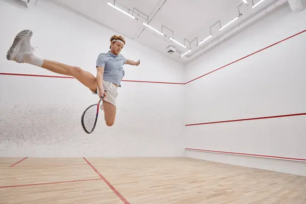 Motion shot, energetic player holding racquet while jumping and playing squash inside of court — Stock Photo