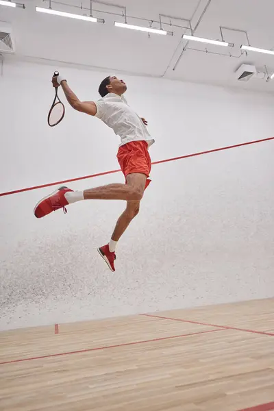 Coup de mouvement, joueur afro-américain motivé tenant la raquette tout en sautant et en jouant au squash — Photo de stock