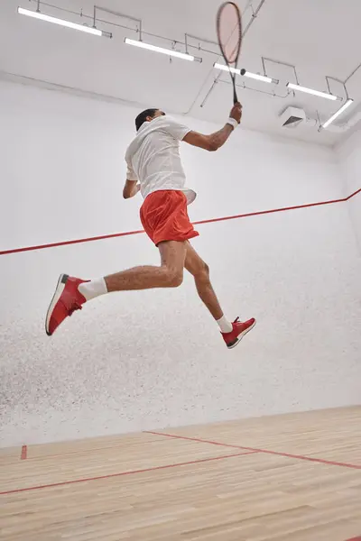 Фото движения, активный африканский спортсмен держит ракетку во время прыжков и игры в сквош — стоковое фото