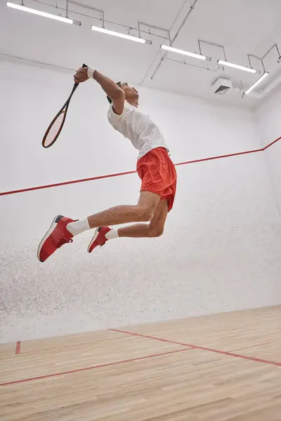 Photo de mouvement, sportif afro-américain actif tenant une raquette tout en sautant et en jouant au squash — Photo de stock