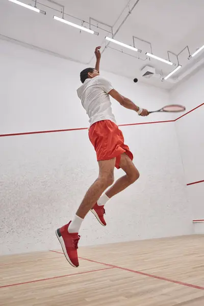 Photo de mouvement, sportif afro-américain actif avec raquette sautant et jouant au squash au tribunal — Photo de stock