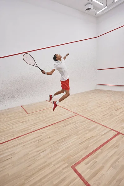 Movimiento, deportista afroamericano activo con raqueta saltando y jugando squash en la corte — Stock Photo