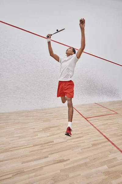 Motion shot, sportif afro-américain concentré avec raquette sautant et jouant au squash au tribunal — Photo de stock
