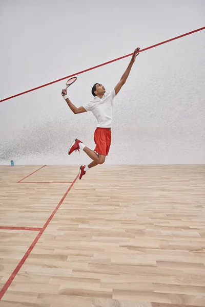 Motion shot, joueur afro-américain concentré avec raquette sautant et jouant au squash au tribunal — Photo de stock