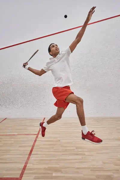 Mouvement, joueur afro-américain concentré avec raquette sautant et regardant la balle, jouant au squash — Photo de stock