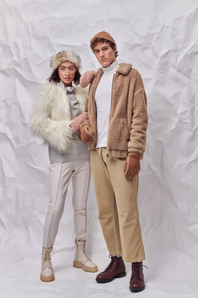 Trendy interracial couple in warm faux fur jackets on white textured backdrop, winter fashion — Stock Photo