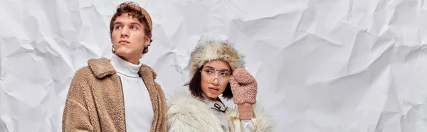 Asiatique femme dans lunettes et fausse fourrure chapeau regardant loin près de l'homme sur blanc froissé barhop, bannière — Photo de stock