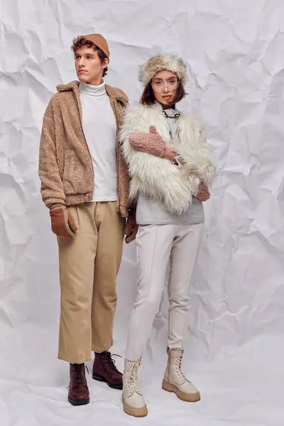 Longitud completa de la pareja multiétnica n traje de invierno de moda sobre fondo de papel blanco arrugado - foto de stock